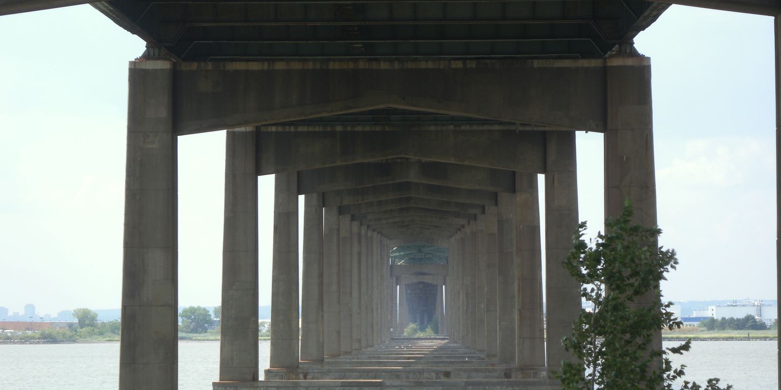 Looking along the underside of a highway bridge over Newark Bay, concrete piers receding into the distance